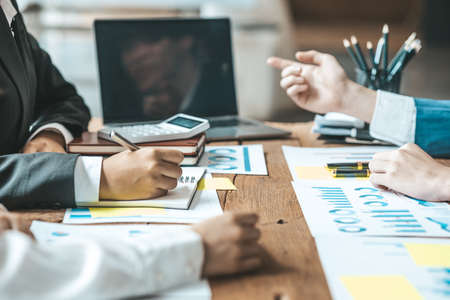 A desk in a company conference room has a group of business people attending and with supporting...