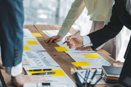 A desk in a company conference room has a group of business people attending and with supporting...