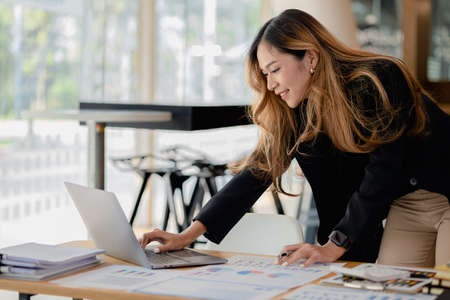 A beautiful Asian businesswoman sitting in her private office, she is checking company financial documents, she is a female executive of a startup company. Concept of financial management.の写真素材