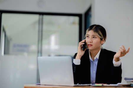 Asian woman talking on the phone, she is a salesperson in a startup company, she is calling customers to sell products and promotions. Concept of selling products through telephone channels.の写真素材