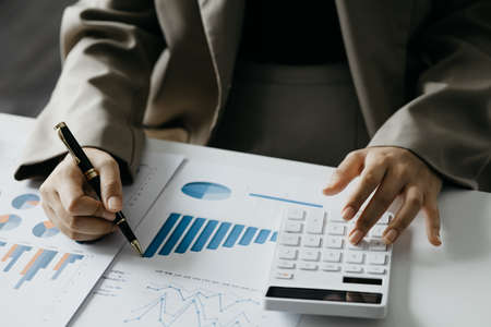 Businessman using a calculator to calculate numbers on a company's financial documents, he is...