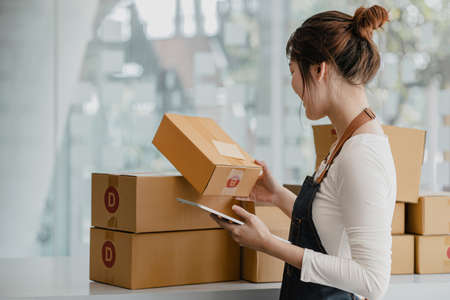 A beautiful Asian business owner opens an online store, she is checking orders from customers,...