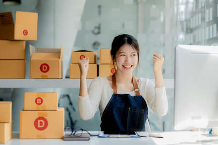 A beautiful Asian business owner opens an online store, she is checking orders from customers, sending goods through a courier company, concept of a woman opening an online business.の写真素材