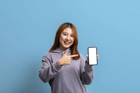 Portrait of beautiful Asian woman holding mobile phone on isolated background, portrait concept used for advertisement and signage, isolated over blue background, copy space.の写真素材