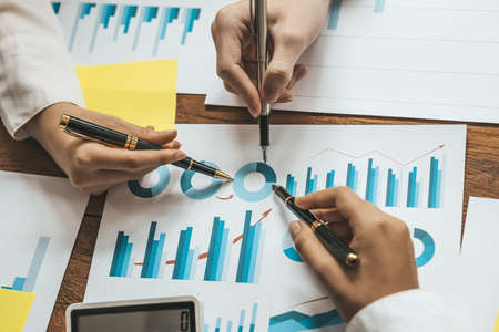 A desk in a company conference room has a group of business people attending and with supporting...