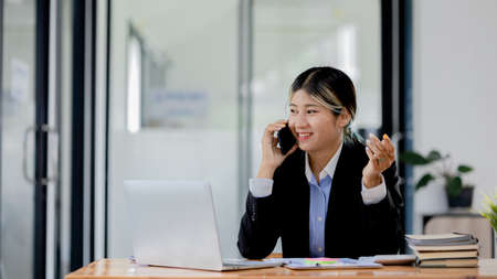 Asian woman talking on the phone, she is a salesperson in a startup company, she is calling...