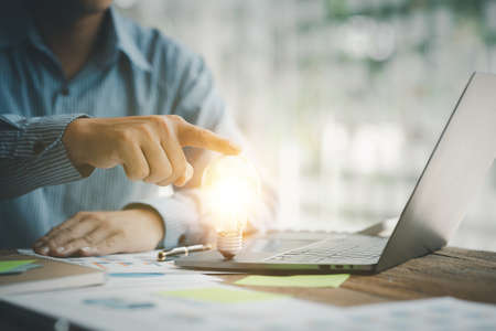 Standing man hold glowing light bulb, Creative new idea. Innovation, brainstorming, strategizing to make the business grow and be profitable. Concept execution, strategy planning and profit managementの写真素材