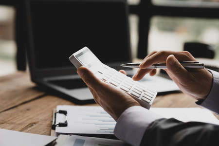 Businessman using a calculator to calculate numbers on a company's financial documents, he is analyzing historical financial data to plan how to grow the company. Financial concept.の写真素材