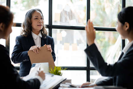 Senior businesswoman with senior executives talking in a meeting, she is meeting with department head staff at a conference room, senior female executives and new generation employees working togetherの写真素材