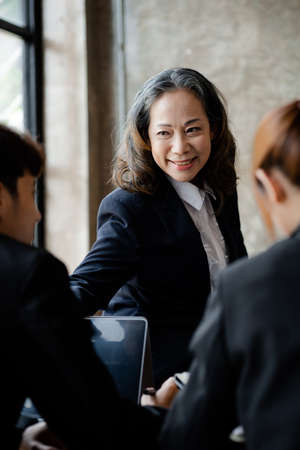 Senior businesswoman with senior executives talking in a meeting, she is meeting with department head staff at a conference room, senior female executives and new generation employees working togetherの写真素材