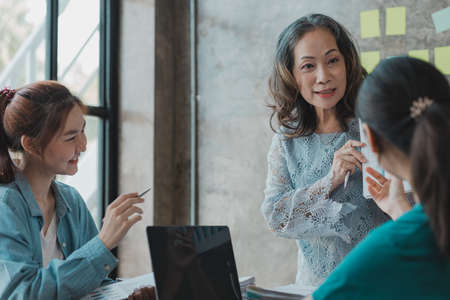 A startup executive is meeting with a new generation of employees to plan and discuss, she is an experienced senior executive with a modern mindset. Management concept of startup company.の写真素材