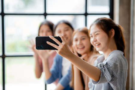 Beautiful Asian woman holding a mobile phone up to take pictures with a group of friends at work, taking pictures using a new smartphone. shooting concept selfie from a smart communication device.の写真素材