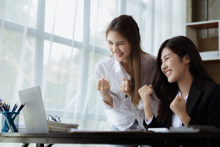Two women showing joy and looking at data on their laptop, two business women looking at a monthly summary of sales that exceed sales targets and achieve profitable growth. Sales management conceptの写真素材
