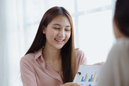 Two beautiful Asian women are meeting together in a company meeting room, meeting to discuss plans to develop the business to grow and follow the business plan. Business meeting idea.の写真素材