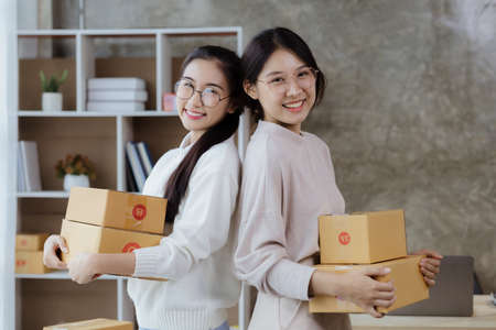 A beautiful Asian business owner opens an online store, she is checking orders from customers, sending goods through a courier company, concept of a woman opening an online business.の写真素材
