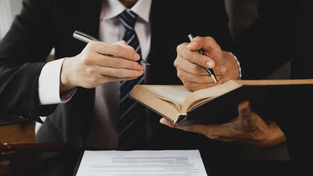 Two lawyers are reading a large book of law to jointly draft a prosecution contract and look at the...