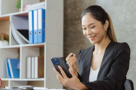 Woman gesturing and looking at mobilephone screen, businesswoman checking company monthly sales and pretending to be happy as sales meet planned targets according to policy. Sales management concept.の写真素材