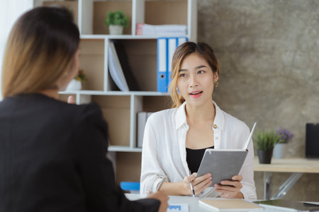 Atmosphere in the office of a startup company, two female employees are discussing, brainstorming ideas to working on summaries and marketing plans to increase sales and prepare reports to managers.の写真素材