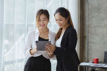Two beautiful Asian women are meeting together in a company meeting room, meeting to discuss plans to develop the business to grow and follow the business plan. Business meeting idea.の写真素材