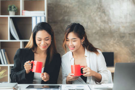 Atmosphere in the office of a startup company, two female employees are discussing, brainstorming ideas to working on summaries and marketing plans to increase sales and prepare reports to managers.の写真素材