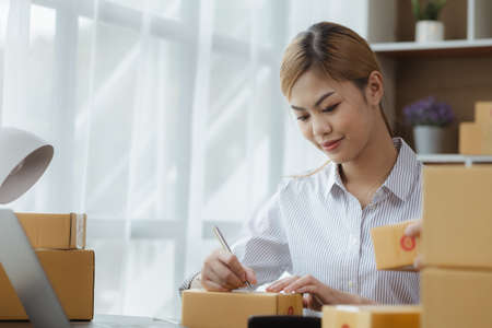 Woman who runs an e-commerce business is writing a list of customers on paper before shipping to...