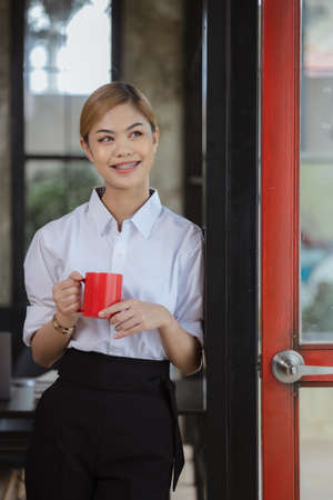 Asian female employee in company office standing holding red coffee cup, energetic young Asian businesswoman founded a new modern management startup company. female leaders running a business Concept.の写真素材