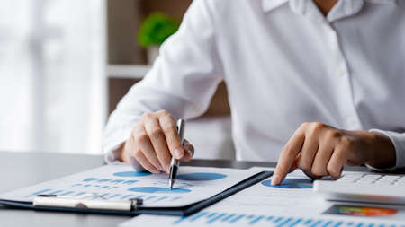 Close-up businesswoman's hand holding a pen pointing at a bar chart on a corporate financial information sheet, the businesswoman examines the financial information provided by the finance department.の写真素材