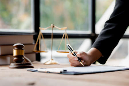 A lawyer sits in his office, on a table with a small hammer to beat the judges desk in court. and justice scales, lawyers are drafting a contract for the client to use with the defendant to sign.の写真素材