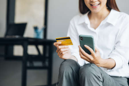 Beautiful woman holding a credit card, she uses a credit card to pay for goods and services online, the concept of using a credit card for online shopping, ordering goods and services on the website.の写真素材