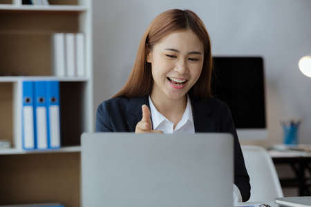 Asian businesswoman looking at laptop screen and remote video call with startup partner, she talks to her friend through program on laptop. Concept of using communication technology.の写真素材