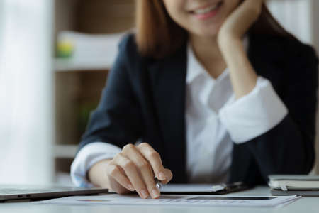 Asian woman looking at documents at a desk in a startup company, she is a financier overseeing the company's finances in accordance with policy and accuracy. Concept of corporate financial management.の写真素材
