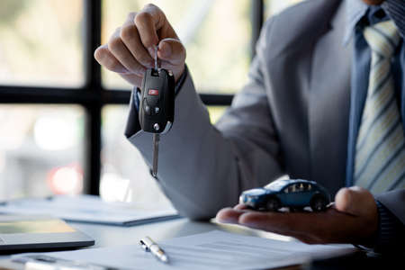 The car salesman hands the key to the customer after discussing the details and signing the purchase...
