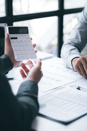 Two businessmen looking at sales data sheets in the office, they are business partners forming a...