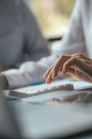 A businessman is using a white calculator to calculate financial numbers, he is sitting in his private office, the businessman examines the financial data from the corporate finance chart.の写真素材