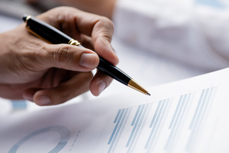 A close-up view of a businessman holding a pen pointing at a bar chart on a company financial...