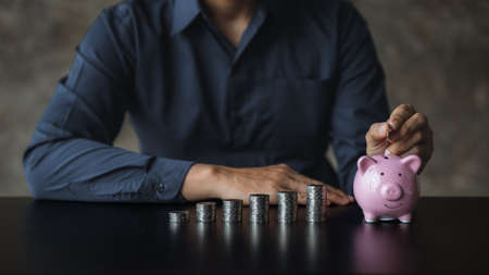 A businessman holding a coin in a piggy bank. Placing coins in a row from low to high is comparable to saving money to grow more. The concept of growing savings and saving by investing in stock funds.の写真素材