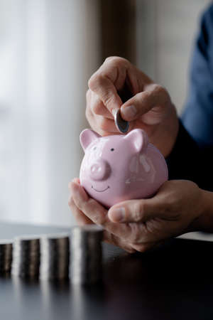 A businessman holding a coin in a piggy bank. Placing coins in a row from low to high is comparable to saving money to grow more. The concept of growing savings and saving by investing in stock funds.の写真素材