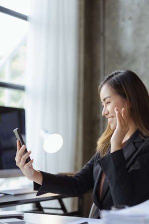 Asian businesswoman looking at smartphone screen and remote video call with startup partner, she talks to her friend through program on smartphone. Concept of using communication technology.の写真素材