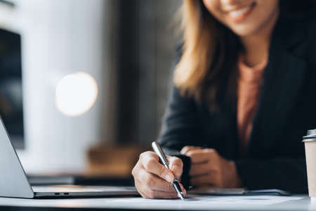 A beautiful Asian businesswoman sitting in her private office, she is checking company financial documents, she is a female executive of a startup company. Concept of financial management.の写真素材