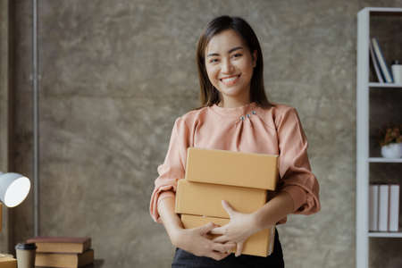 A beautiful Asian business owner opens an online store, she is checking orders from customers, sending goods through a courier company, concept of a woman opening an online business.の写真素材
