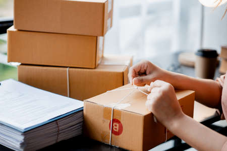 An Asian woman tying a parcel to a customer's box, she owns an online store, she packs and ships through a private transport company. Online selling and online shopping concepts.の写真素材