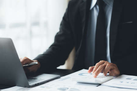 Businessman is using a calculator to calculate company financial figures from earnings papers, a...