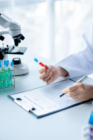 A laboratory assistant, a medical scientist, a chemistry researcher holds a test tube of chemicals and examines the disease from a patient's blood sample. Medicine and research concept.の写真素材