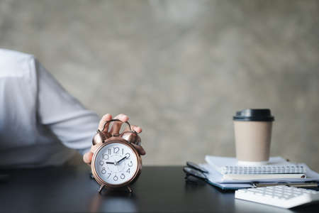 A person's hand presses the desk clock to turn off the alarm, he is lying down during a break during work hours to relax. The idea of taking a break during the working day.の写真素材
