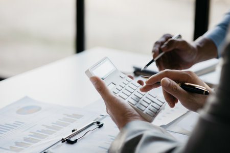 Business man using a white calculator, a financial businessman examining the numerical data on a company financial document, he uses a calculator to verify the accuracy of numbers.の写真素材