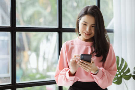 Asian woman working in a startup company, she is using the phone. run by a young, talented woman. The management concept runs the company of female leaders to grow the company.の写真素材