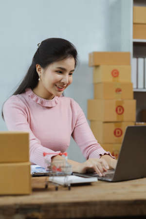 A beautiful Asian business owner opens an online store, she is checking orders from customers,...