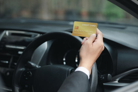 An Asian man in a formal suit is in a car, he holds a credit card, he drives into a gas station and pays his credit card bills, travel by car, safe driving, respecting traffic rules.の写真素材