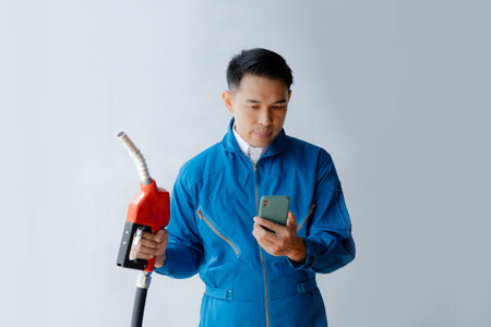 Asian man holding a gas nozzle and mobile phone, fuel consumption, petrol cars, fluctuating oil...