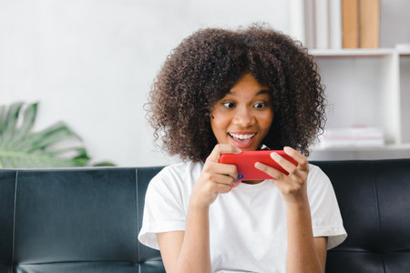 An American woman sits on the sofa on her smartphone, spends her weekends on social media, watching...